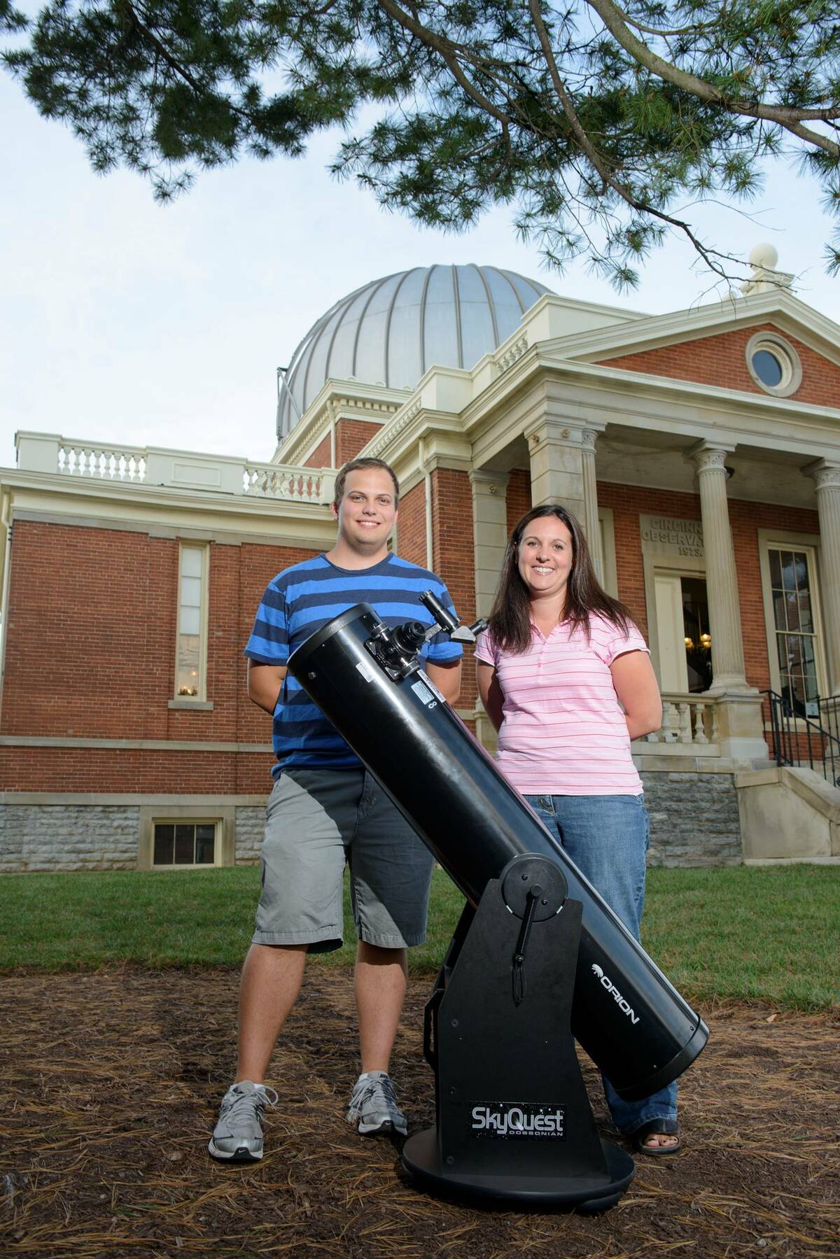 Two people standing behind a telescope